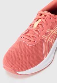 Scarpa da corsa rosa corallo con tomaia in rete, lacci a fantasia, accenti arancioni chiari e suola bianca imbottita, inclinata per mostrare i dettagli frontalmente e lateralmente.
