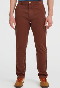 Bruine katoen chino's met een rechte pasvorm, voorzien van een knoopsluiting, zijzakken en subtiele stikdetails. Gecombineerd met tan sneakers.