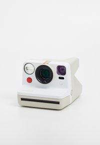 Appareil photo instantané Polaroid, corps blanc, design arrondi, objectif vert, bouton rouge, classique bande arc-en-ciel sur le dessus, fente pour film à l'avant.