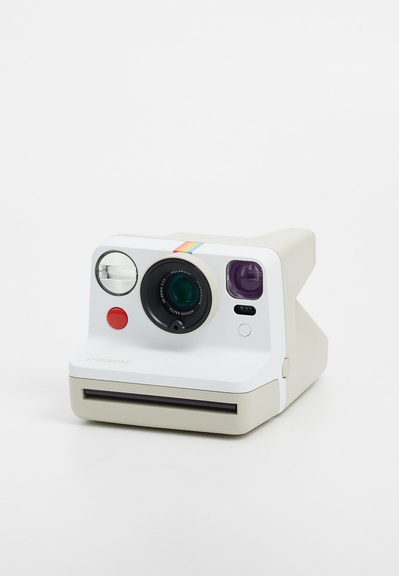 Appareil photo instantané Polaroid, corps blanc, design arrondi, objectif vert, bouton rouge, classique bande arc-en-ciel sur le dessus, fente pour film à l'avant.