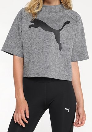 Frau trägt ein graues, kurz geschnittenes Puma-T-Shirt mit schwarzem Puma-Logo und schwarze Leggings mit kleinem weißem Puma-Logo.