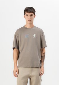 Grå bomulds T-shirt med korte ærmer, prydet med trykt tekst i blå og hvid. Rund halsudskæring og afslappet pasform. Simpelt design uden mønstre.