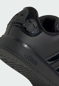Black sneaker made of synthetic materials. Features Star Wars character accents, textured sole, and three stripe design on the side.