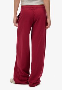 Bordeaux brede sweatpants van zacht materiaal, met een elastische tailleband en zijzakken. Glad textuur met een ontspannen pasvorm.
