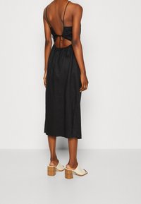 Svart midiklänning med låg rygg och justerbar knytning. Har tunna axelband och en avslappnad passform, tillsammans med krämfärgade öppen-tå hälar.
