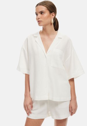 Witte oversized korte mouwen knoop blouse met een zak, gemaakt van lichte stof, gecombineerd met bijpassende shorts.