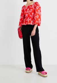 Czerwona bluzka peplum w kwiaty z długimi rękawami, czarne szerokie spodnie i różowe sandały na platformie z warstwową podeszwą. Nosi małą czerwoną torbę.