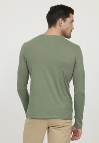 Chemise à manches longues, col rond en coton mélangé vert olive, avec une texture lisse, une coupe ajustée et un ourlet simple sans logos visibles.
