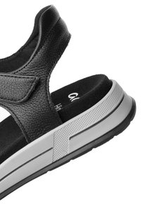 Black sandals with a textured leather upper, padded strap, and grey rubber sole featuring a grip pattern. Velcro closure for adjustable fit.