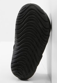 Svart gummisula med ett vågigt mönster, med spår för grepp och en texturerad yta för hållbarhet.