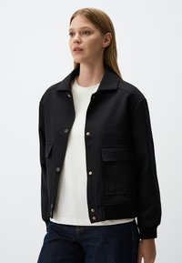 Veste bomber noire en tissu lisse, avec un col, des boutons-pression, deux poches avant et des poignets côtelés.