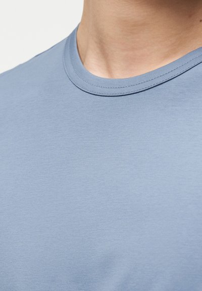 Κοντινό πλάνο του λαιμού και του άνω μέρους του στήθους ενός ατόμου που φοράει ένα απλό γαλάζιο T-shirt με στρογγυλή λαιμόκοψη.