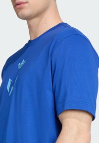 Blue cotton t-shirt with short sleeves, crew neck, and a light blue graphic design on the front, featuring an abstract pattern.