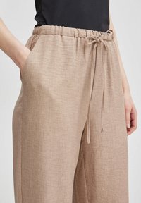 Ljusbruna linbyxor med ett elastiskt midjeband och dragsnören samt sidofickor. Tyget har en diskret struktur.
