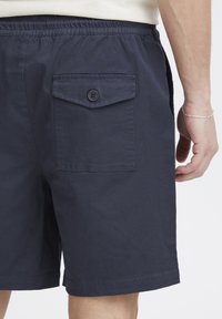 Tengerészkék rövidnadrágok könnyű szövetből, elasztikus derékrésszel, oldalzsebekkel és gombos, fedeles hátzsebbel.