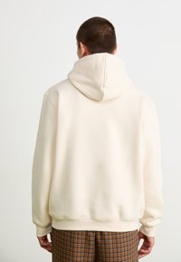 Sweatshirt capuz em bege claro com um ajuste descontraído, apresentando um bolso canguru e punhos canelados. Textura suave; design minimalista.