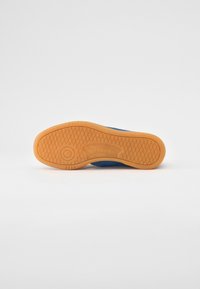 Adidași albaștri cu o talpă din cauciuc gumos. Prezintă modele texturate și un logo Reebok pe mijlocul tălpii. Design elegant și funcțional.