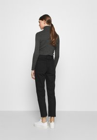 Crne hlače visokog struka s uskim krojem, manžetama na rubovima i dva stražnja džepa, u kombinaciji s sivim rebrastim turtleneckom i bijelim tenisicama.