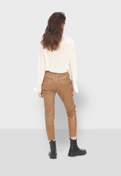 Pantalons en cuir marron avec une taille élastique, associés à une chemise à manches longues crème. Des bottines noires épaisses complètent le look.