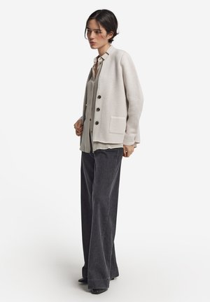 Lys beige strikket cardigan med rund hals, lange ærmer, frontknapper og lomme. Sættes sammen med en grå skjorte med knapper og mørke brede bukser.