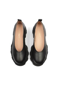 Zapatos negros de cuero sin cordones con punta redondeada, suela de goma gruesa y diseño minimalista. Cuenta con un pequeño tirador en el talón para facilitar su uso.
