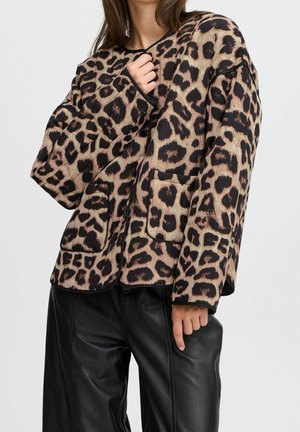 Kvinde iført en løs leopardprintjakke med store forlommer og sorte læderbukser mod en ensfarvet baggrund.