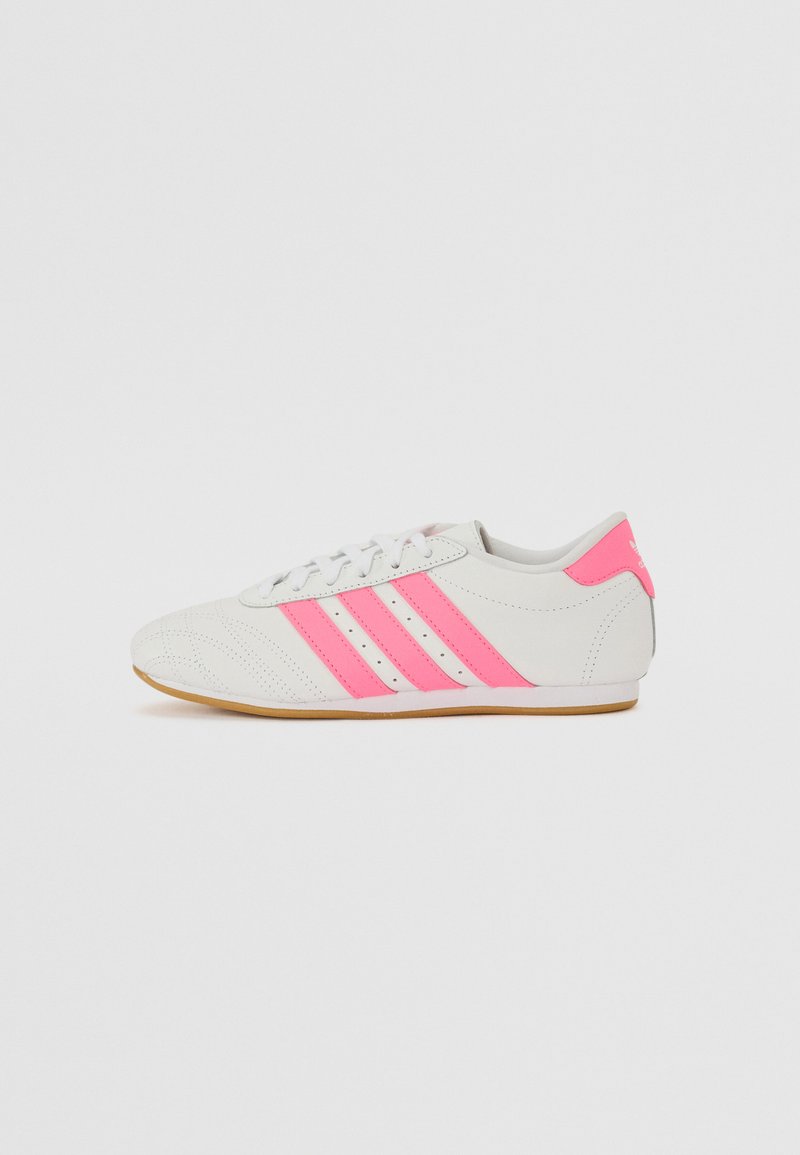 Tênis atléticos brancos com detalhes em rosa e três riscas rosas de lado, apresentando um cabedal texturizado e sola de borracha.