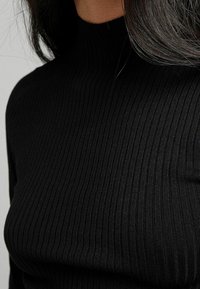 Haut col roulé côtelé noir avec une coupe ajustée, présentant des lignes verticales et une texture lisse, mettant en valeur un col haut.