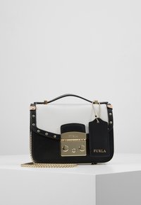 Borsa a mano in pelle bianca e nera con chiusura in metallo dorato, tracolla a catena, dettagli con borchie e una targhetta. Forma rettangolare compatta.