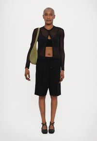 Black sheer long-sleeve cardigan with button closure, revealing a black crop top. Paired with black tailored shorts and black shoes. Green bag.