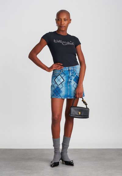 Camiseta negra ajustada con logo, minifalda de mezclilla con parches azules, calcetas grises hasta la rodilla, zapatos planos negros de punta y un pequeño bolso negro.