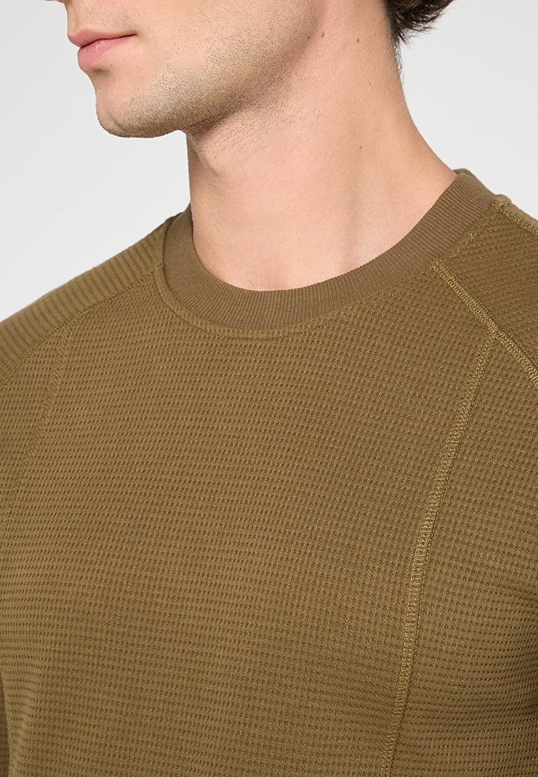 Olivgrüner, strukturierten Strickpullover mit Rundhalsausschnitt und Raglanärmeln. Der Stoff wirkt weich und zeigt sichtbare Nähte.