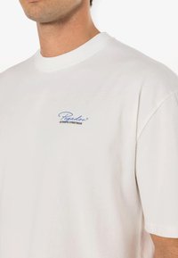Balta trumpa rankovėmis marškinėliai, pagaminti iš medvilnės, su šviesiai mėlynu logotipu, kuriame yra „Pegador“ ir „AUTHENTIC STREETWEAR“ juodu tekstu ant krūtinės.