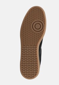 Schwarze Sneaker mit einer strukturierten Gummisohle, die ein kreisförmiges Design und ein Zickzackmuster aufweist. Die Unterseite zeigt eine glatte, stabile und flexible Oberfläche.