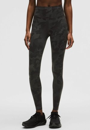 Mørke leggings med camouflage mønster båret med sorte løbesko, vist fra mellemgulv til fødder på neutral baggrund.