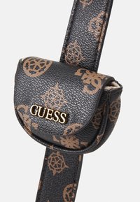 Malá černá kožená taštička s texturou, hnědými námořnickými vzory a zlatým logem GUESS na přední straně, připevněná k odpovídajícímu popruhu.