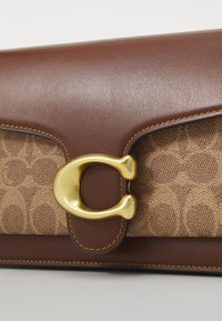 Brown leather clutch with a textured tan fabric featuring a pattern. Gold-tone hardware accentuates the design, highlighting the closure detail.