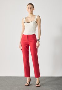 Haut structuré blanc avec des finitions noires associé à un pantalon rouge sur mesure. Des sandales noires à lanières complètent le look. Tissu lisse avec des lignes épurées.