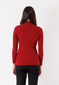 Maglietta a maniche lunghe a coste rossa con collo alto e silhouette aderente, abbinata a pantaloni neri.