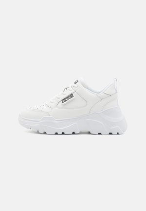 Baskets blanches chunky avec une semelle en caoutchouc texturé, un dessus en cuir et des détails perforés. Présente un logo sur le côté et une languette à l'arrière.