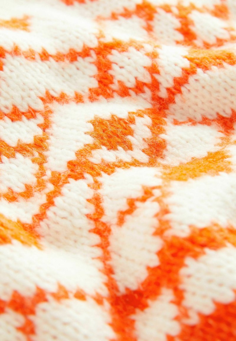 Strickstoff mit einem orange-weißen geometrischen Muster. Das Material sieht weich aus, hat eine strukturierte Oberfläche und einen klaren Farbkontrast.