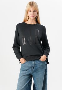 Black sweatshirt with prominent glossy "GAP" logo, round neck, long sleeves, and ribbed cuffs, paired with light blue wide-leg jeans.