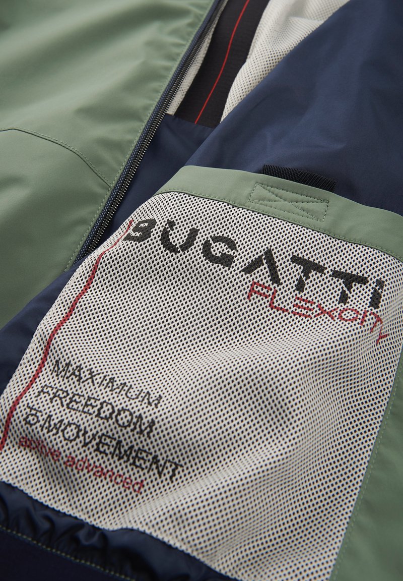 Veste Bucatti Flexion avec un design vert et marine. Comprend un tissu en mesh, des coutures visibles et du texte imprimé sur une surface texturée.