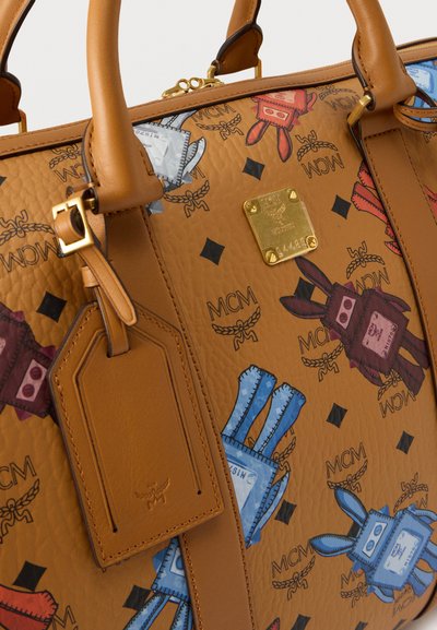 Sac à main en cuir caramel avec des imprimés colorés de lapins cartoon, plaque logo MCM en or et étiquette de bagage en cuir avec détail de sangle à boucle.