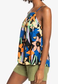 Débardeur floral en bleu, orange et vert, offrant une coupe ample, des bretelles fines et un design plissé. Associé à un short vert olive.