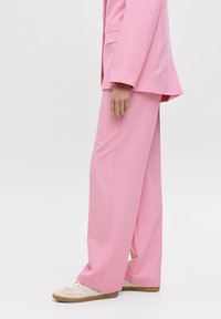 Roze tailleursuit met wijde broekspijpen en een bijpassende blazer, gemaakt van zachte stof, in combinatie met crème sneakers.