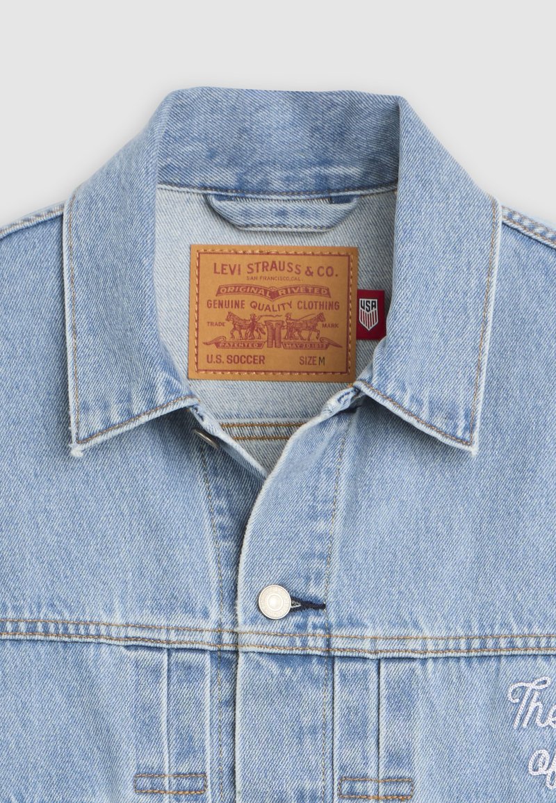 Col de veste en denim bleu clair avec étiquette beige Levi Strauss & Co., bouton argenté et petite étiquette rouge USA à l'intérieur au niveau de la nuque.