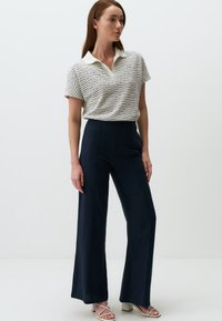 Koszulka polo z krótkim rękawem o wzorze w białe i granatowe pasy, zestawiona z granatowymi spodniami o wysokim stanem i szerokich nogawkach. Sandały na obcasie z odkrytymi palcami.