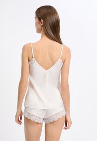 Satynowa koszulka na ramiączkach w jasnym beżu z regulowanymi paskami i koronkowymi zdobieniami; zestawiona z dopasowanymi szortami z falistą koronkową lamówką.