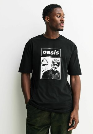 Schwarzes Baumwoll-T-Shirt mit einem grafischen Druck von zwei Figuren in Schwarz-Weiß. Das Design beinhaltet das Wort "oasis" in fetten Buchstaben.